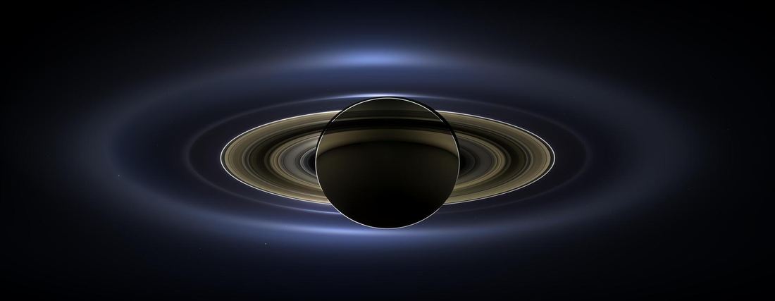 Saturn backlit by the Sun with its rings glowing, and Earth visible as a tiny dot in the distance